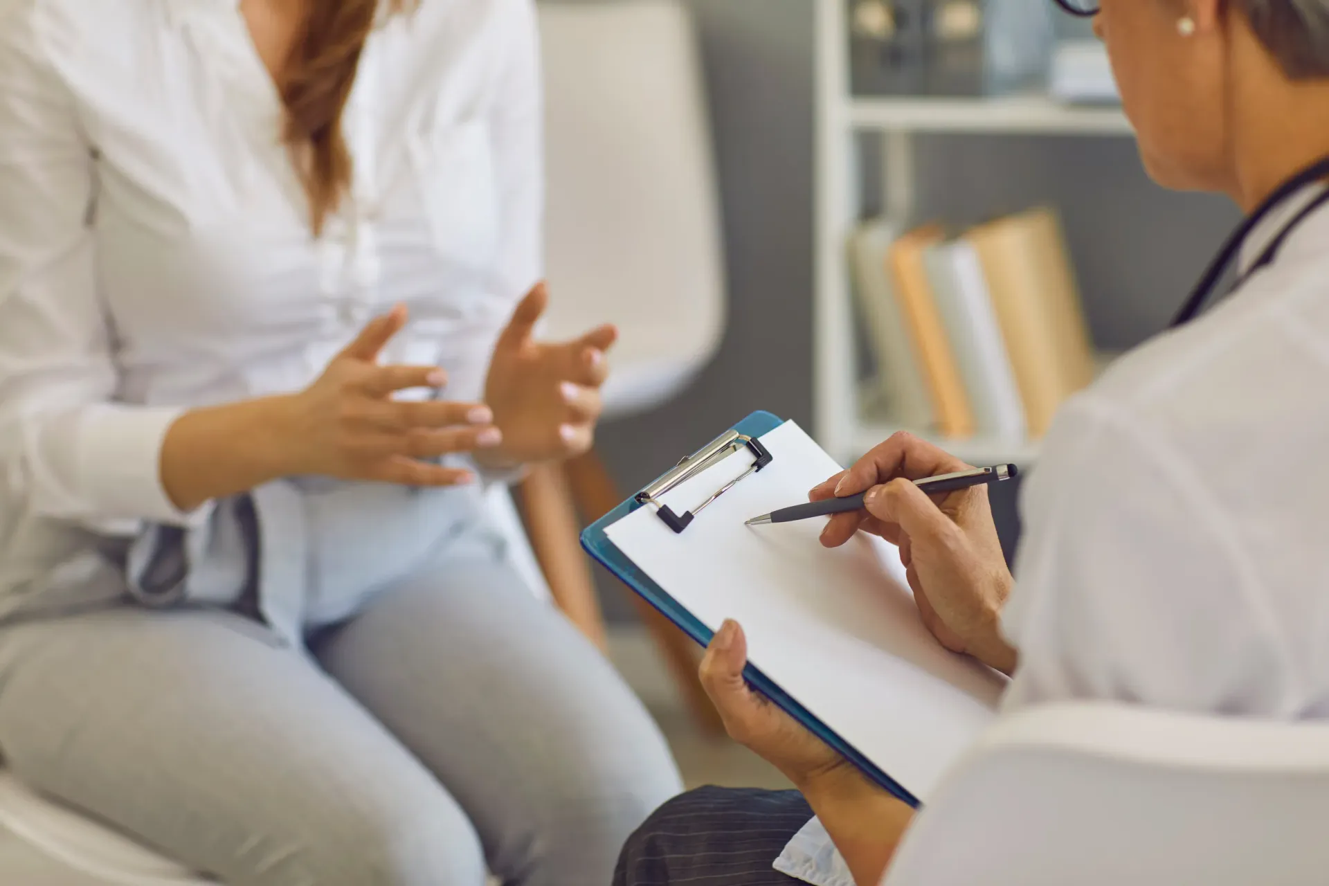 Terapeuta tomando notas mientras habla con un paciente sentado en una oficina luminosa.