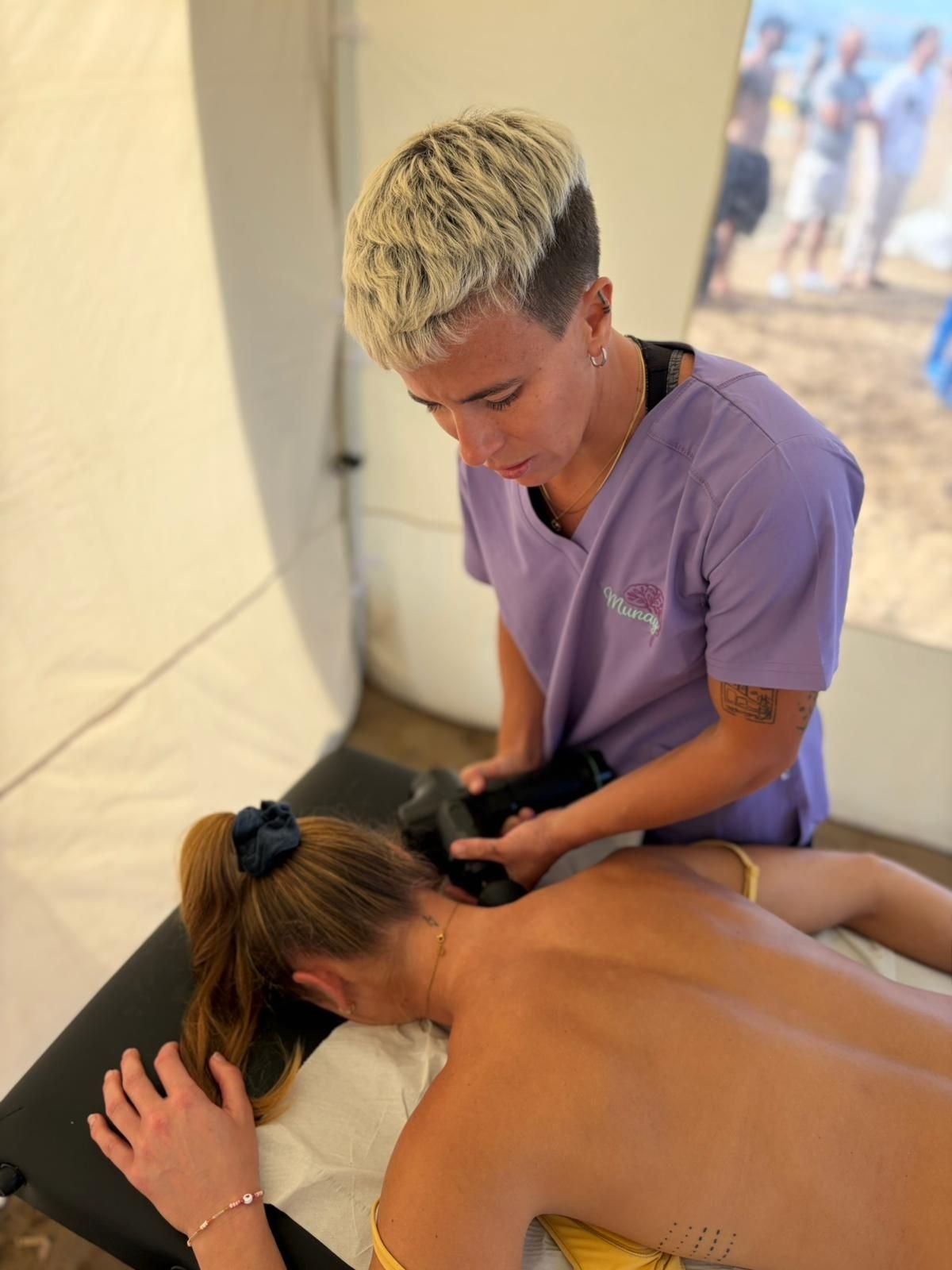 Masajista amasando la espalda de un cliente dentro de una tienda de campaña con una camisa morada y guantes negros.